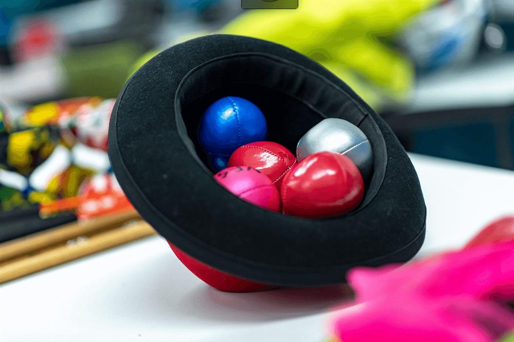 an upturned hat containing 5 colourful juggling balls