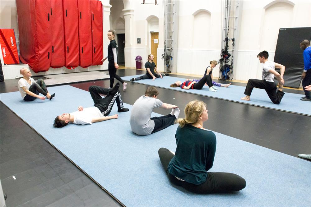A small group of people bending forwards with their hands on the floor with one leg in the air behind them