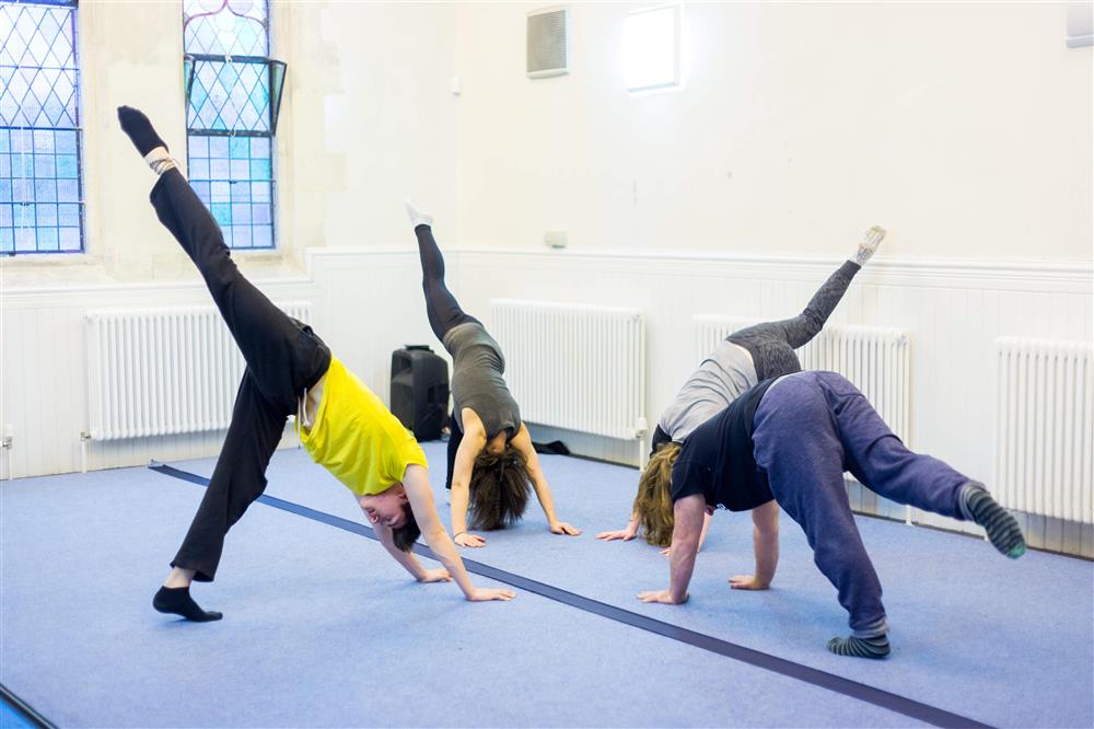 A small group of people bending forwards with their hands on the floor with one leg in the air behind them